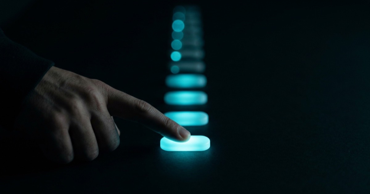 A fingertip tapping the first in a receding trail of glowing cyan answer buttons in darkness — one small yes at a time.